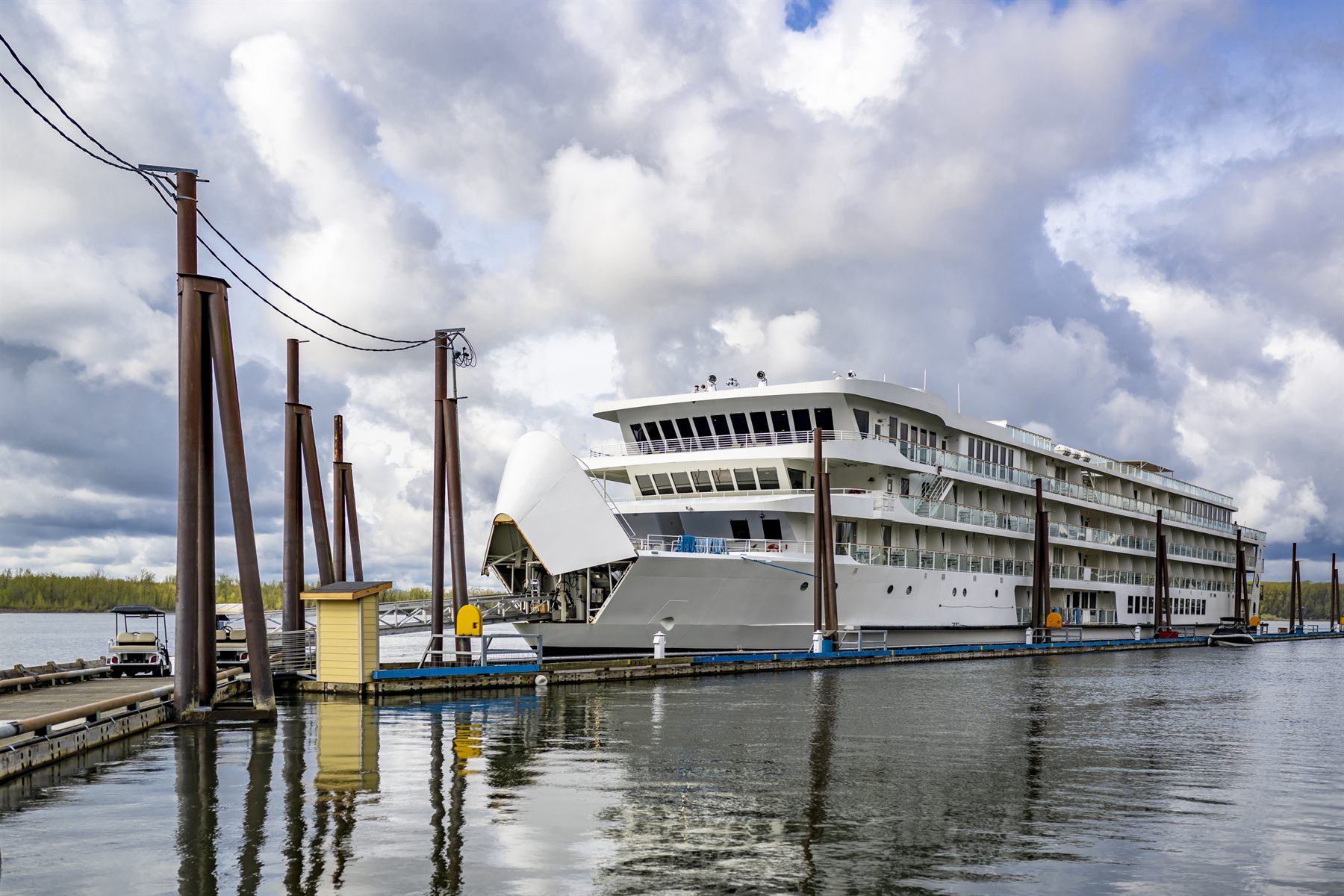 Modern white riverboat moored at a wooden dock under a cloudy sky