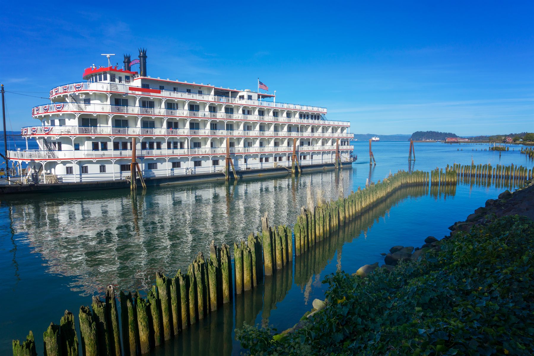 Paddlewheel riverboat moored beside rows of old wooden pier pilings on a wide river